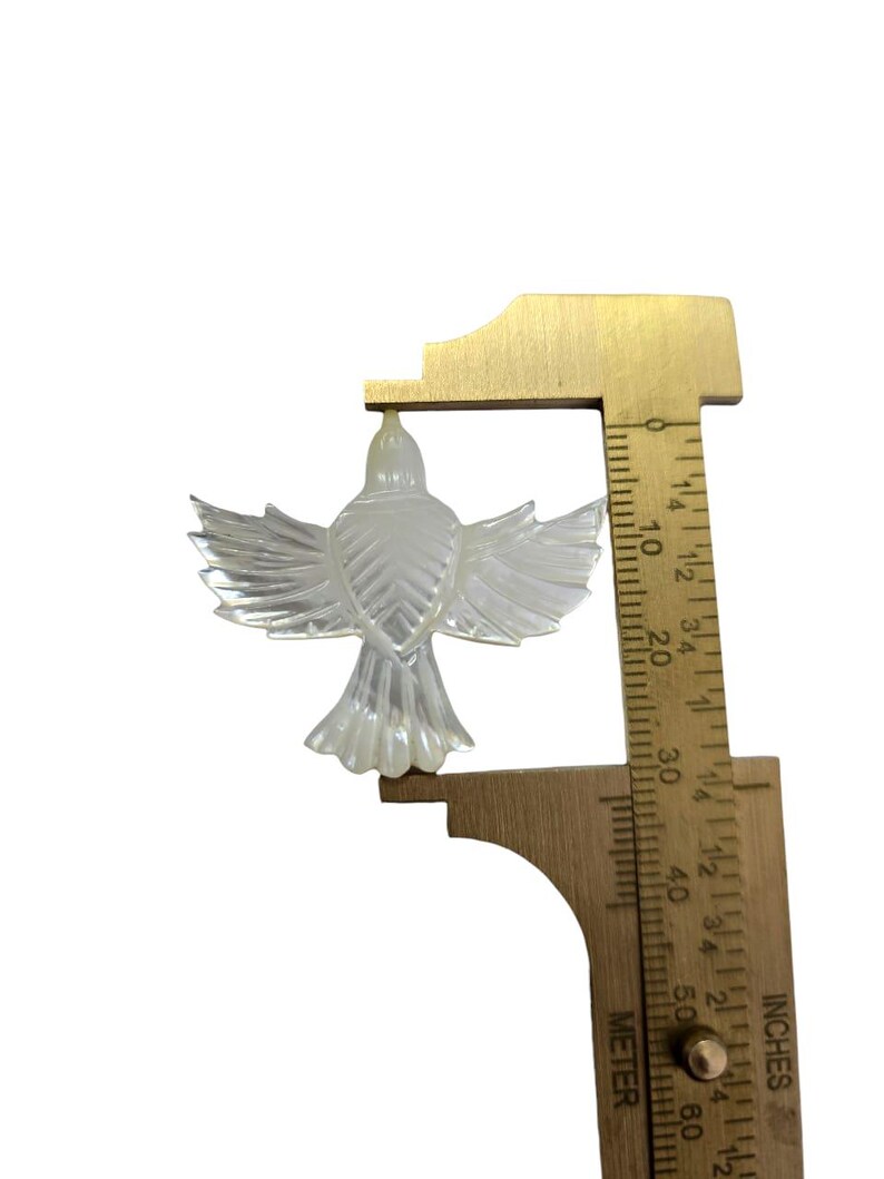 May include: A clear, iridescent bird-shaped ornament with outstretched wings. The ornament is being measured with a ruler, showing a height of approximately 2 inches. The bird has detailed feather patterns and a textured surface.