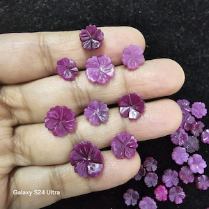 以下が含まれることがあります： ピンクとパープルの花の形をした宝石のコレクション。宝石は複雑なディテールで彫刻されており、磨かれた仕上げになっています。