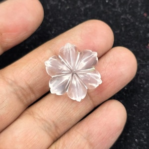 K&ouml;nnte beinhalten: Eine klare Quarzblume, die in Form einer zarten Blume geschnitzt ist. Die Blume hat f&uuml;nf Bl&uuml;tenbl&auml;tter und einen Mittelpunkt.