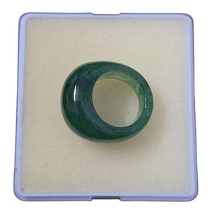 May include: A dark green jade ring with a smooth, polished surface. The ring is circular and appears to be a solid band of jade. The ring is set against a light beige background within a clear plastic case.