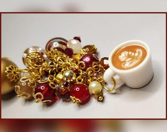 May include: A charm bracelet with a coffee cup charm and a collection of gold-toned chains and beads. The beads are in shades of red, gold, and clear, with a small white coffee cup charm featuring latte art.