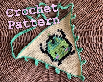 May include: A crocheted triangle with a cartoon monster design. The monster is green and black, with pink accents. The triangle is cream-colored, with green trim and ties. The words "Crochet Pattern" are written across the top.