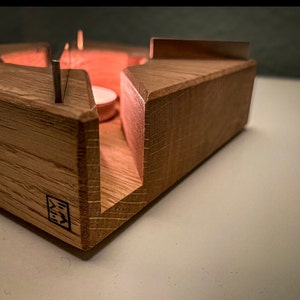 Könnte beinhalten: Ein dreieckiger Kerzenhalter aus Holz mit einer kleinen Kerze in der Mitte. Der Halter hat eine dunkelbraune Farbe und eine hellbraune Holzmaserung. Die Kerze ist angezündet und leuchtet.