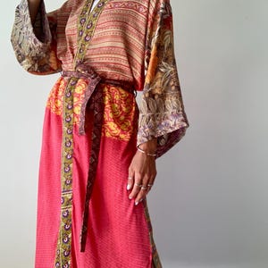 Könnte beinhalten: Ein farbenfrohes Kimono-Kleid mit Muster. Das Kleid weist eine Mischung aus Farben auf, darunter Koralle, Rot, Gelb und Braun, mit komplizierten floralen und geometrischen Designs. Es hat weite Ärmel und einen passenden Gürtel und bietet einen fließenden, eleganten Look.