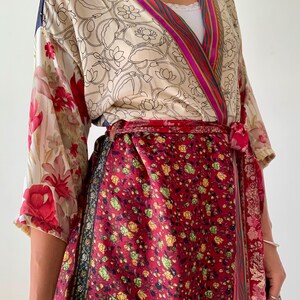 May include: A wrap-style kimono with a floral pattern in red, cream, and pink. The kimono features a red floral skirt and a cream-colored top with black line drawings of flowers. The sleeves have a red floral pattern.