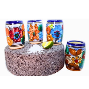 Puede incluir: Cuatro vasos de chupito de cerámica coloridos con diseños florales. Los vasos están dispuestos sobre una superficie de piedra gris con una rodaja de lima y sal.
