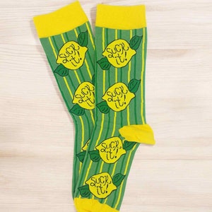 Könnte beinhalten: Ein Paar grüne und gelbe Socken mit einem Zitronenmotiv und dem Text "SUCK IT!" wiederholt auf jeder Socke.
