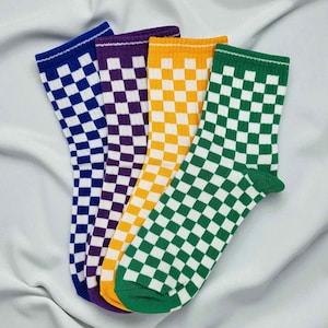 May include: Four pairs of crew socks in a variety of colors: blue, purple, yellow, and green. Each pair features a checkered pattern in white and the sock's primary color. The socks are displayed on a white, textured surface.