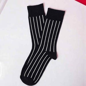 May include: A pair of black socks with vertical white stripes. The socks are folded and displayed on a white surface, with a red accent in the background. The socks are a classic design.