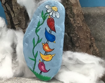 Funny colorful bird pyramid with flower on a stone / natural stone / river stone on a blue background