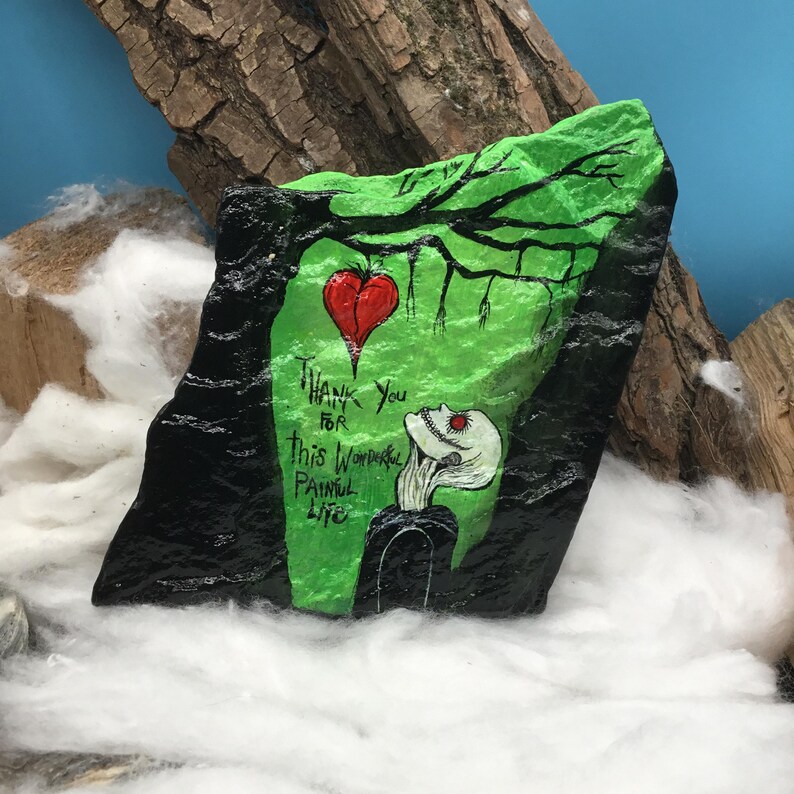May include: Hand-painted rock art featuring a green and black design with a red heart and a skeletal figure. The text reads "Thank You for this Wonderful Painful Life."