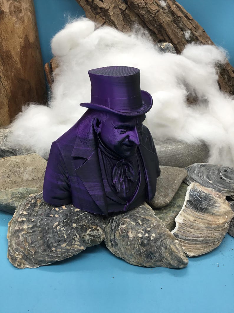 May include: A purple bust of a man in a top hat and suit, set on rocks and oyster shells. The background features cotton and driftwood. The figure has a serious expression. The bust is a decorative item.
