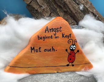 A ladybug with the inscription "Fear begins in the mind, so does courage," hand-painted and immortalized on a natural stone.