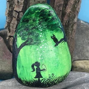 K&ouml;nnte beinhalten: Handbemalter Stein mit einer Darstellung eines M&auml;dchens, das eine Laterne in einem gr&uuml;nen Wald h&auml;lt, mit einer schwarzen Silhouette einer Eule, die auf einem Ast sitzt. Die Laterne strahlt wei&szlig;e Lichtpunkte aus.