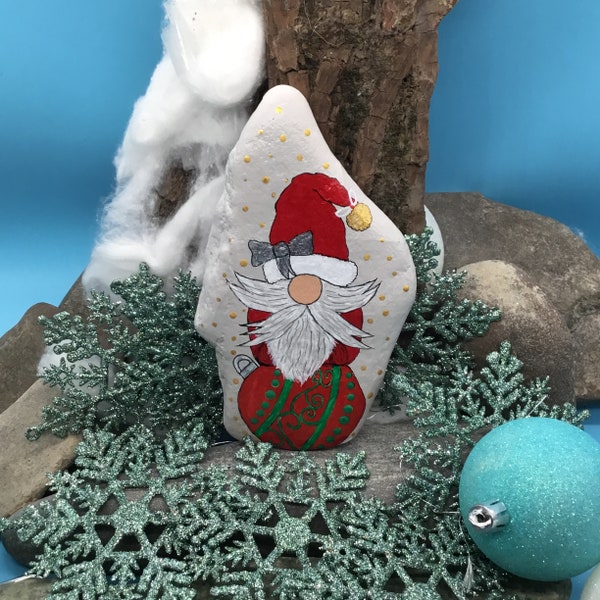 Weihnachts Wichtel mit roter Mütze auf einer Weihnachtskugel sitzend, auf einem  Naturstein gemalt und verewigt.