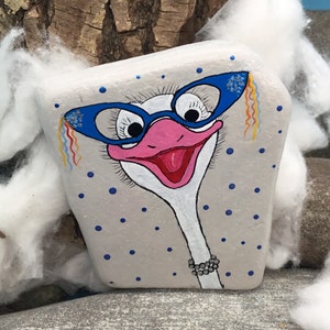 May include: A painted rock with a white background and blue polka dots. The rock depicts an ostrich with blue glasses, a pink beak, and a black beaded necklace.
