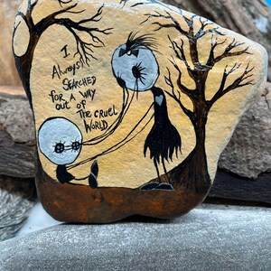 Peut inclure: Galet peint &agrave; la main avec le texte "I Always Searched for a Way Out of the Cruel World". Le design pr&eacute;sente des personnages stylis&eacute;s et des arbres, sur un fond chaleureux. Une &oelig;uvre d'art unique.