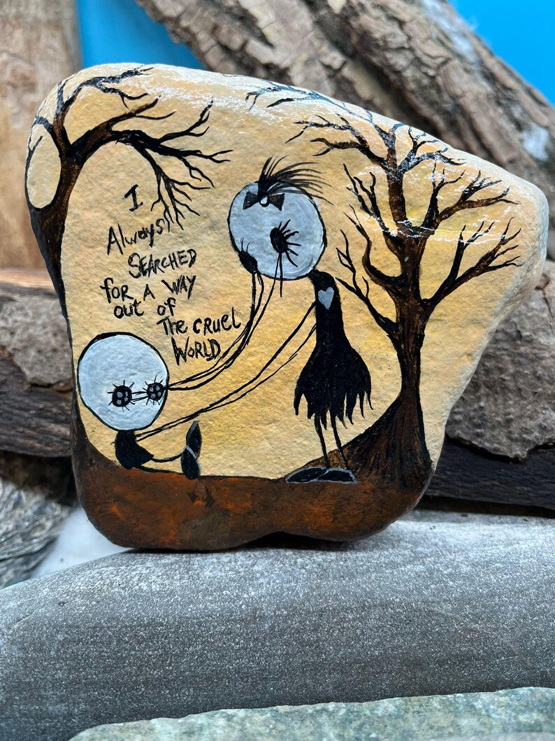 Peut inclure: Galet peint &agrave; la main avec le texte "I Always Searched for a Way Out of the Cruel World". Le design pr&eacute;sente des personnages stylis&eacute;s et des arbres, sur un fond chaleureux. Une &oelig;uvre d'art unique.