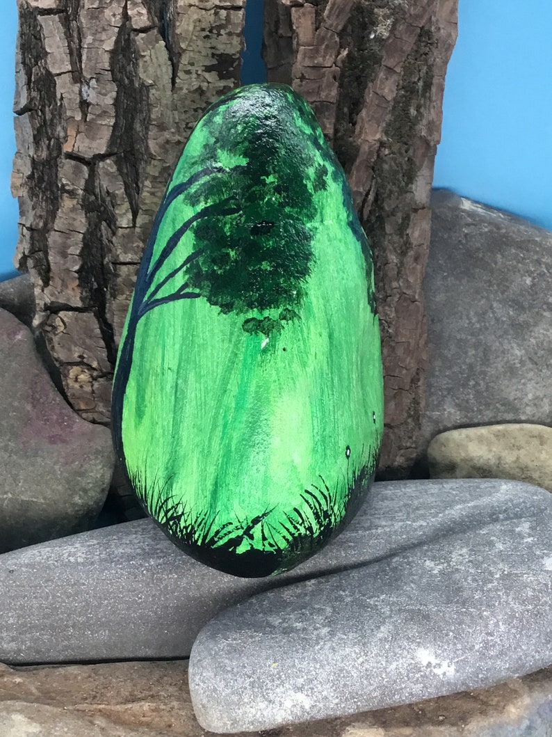 K&ouml;nnte beinhalten: Ein handbemalter Stein mit gr&uuml;nem Hintergrund und einer schwarzen Silhouette eines Baumes. Der Stein ist glatt und oval.