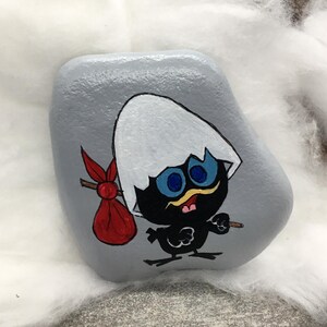 K&ouml;nnte beinhalten: Handbemalter Stein mit einer Cartoon-K&uuml;ken-Figur. Das K&uuml;ken, mit einem zerbrochenen Eierschalenhut, tr&auml;gt einen roten Sack und einen Stock. Der Stein ist grau bemalt, und das K&uuml;ken hat blaue Augen und einen gelben Schnabel.