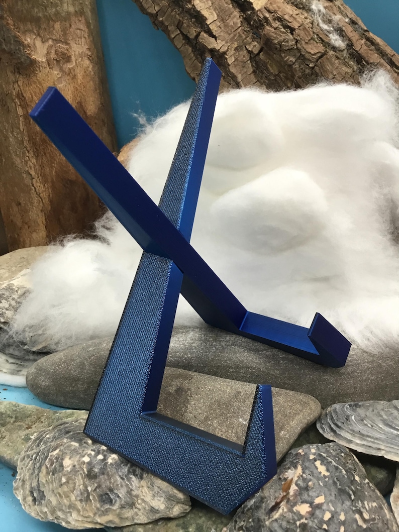 May include: A blue metal display stand with a textured finish. The stand is designed to hold an item and is supported by a base. The stand is made of metal and has a modern design.