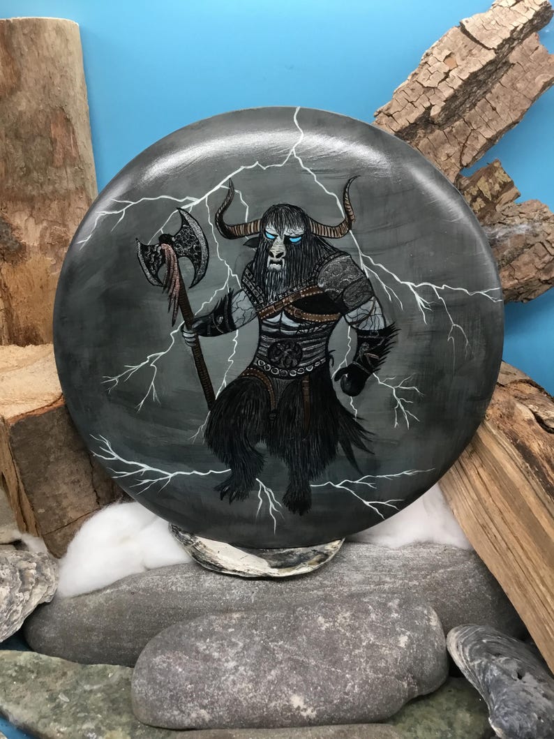 May include: A circular, grey decorative item depicting a minotaur warrior with an axe, set against white lightning bolts. The minotaur has black fur, horns, and blue eyes. The artwork is on a stone-like surface.