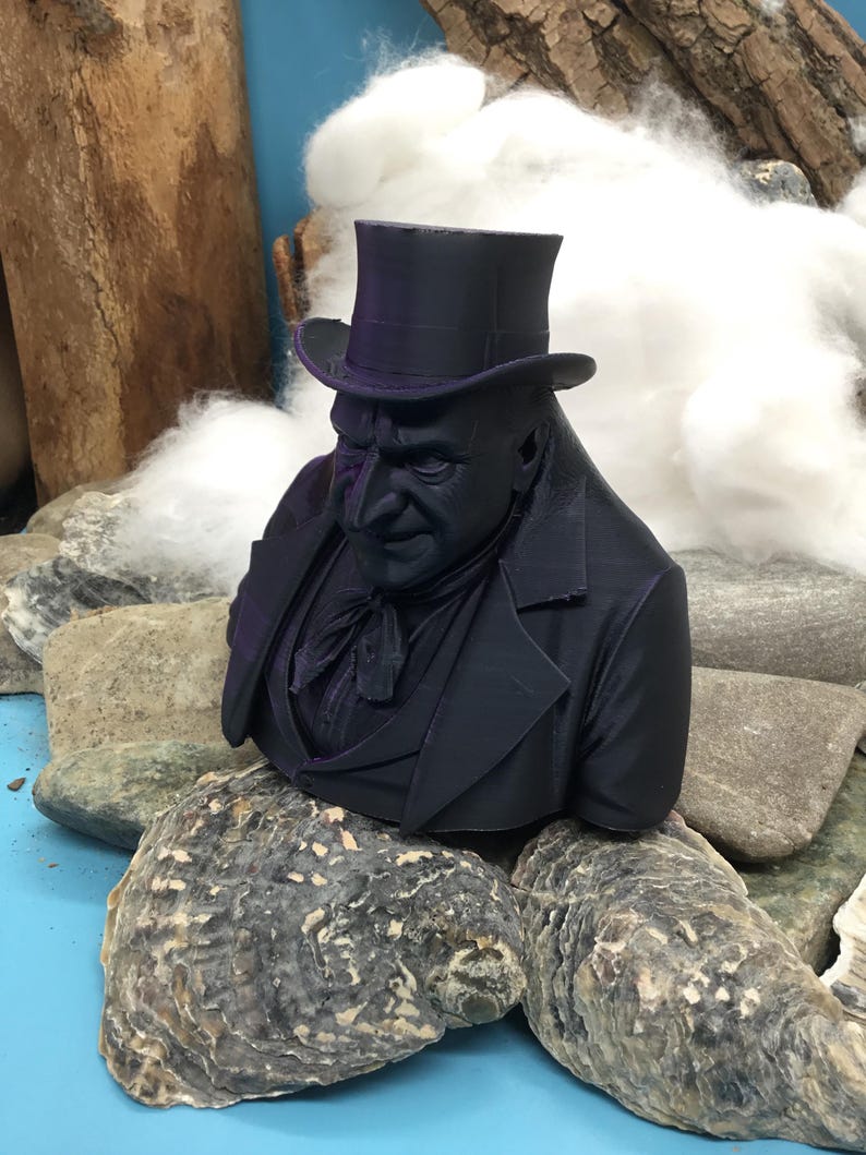 May include: A dark purple bust of a man in a top hat and formal wear. The sculpture is placed on rocks and oyster shells, with wood and cotton in the background. The bust has detailed facial features and clothing.