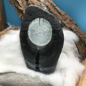 Pu&ograve; includere: Una pietra nera dipinta a mano con un'apertura circolare che raffigura una figura silhouette in piedi nell'acqua sotto un cielo illuminato dalla luna. L'opera d'arte &egrave; ambientata su uno sfondo di cotone bianco e un pezzo di legno.