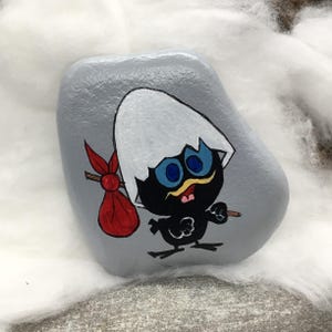 K&ouml;nnte beinhalten: Handbemalter Stein mit einer Cartoon-K&uuml;ken-Figur. Das K&uuml;ken ist schwarz mit blauen Augen, einem gelben Schnurrbart und einer roten Tasche. Der Stein ist grau und das K&uuml;ken schl&uuml;pft aus einer zerbrochenen Eierschale.