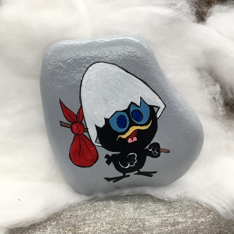 K&ouml;nnte beinhalten: Handbemalter Stein mit einer Cartoon-K&uuml;ken-Figur. Das K&uuml;ken ist schwarz mit blauen Augen, einem gelben Schnurrbart und einer roten Tasche. Der Stein ist grau und das K&uuml;ken schl&uuml;pft aus einer zerbrochenen Eierschale.