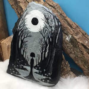 May include: Hand-painted rock art featuring a grayscale forest scene with a silhouetted figure. A large white moon with a black center dominates the sky. The artwork includes detailed trees and a path, creating a mystical, fantasy theme.