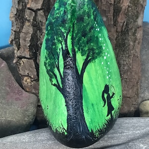 K&ouml;nnte beinhalten: Handbemalter Stein mit einer Darstellung eines gr&uuml;nen Baumes mit schwarzem Stamm und einer kleinen Figur, die davor steht. Der Hintergrund ist ein gr&uuml;ner Farbverlauf mit wei&szlig;en Punkten.
