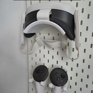 Puede incluir: Un casco de realidad virtual Meta Quest blanco y controladores montados en una tabla perforada IKEA SKÅDIS blanca. El casco es negro y blanco, y los controladores son blancos con tapas negras. El texto "Meta Quest Ikea SKÅDIS mount" está en la parte superior.