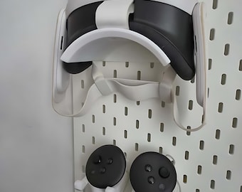 Könnte beinhalten: Ein weißes Meta Quest VR-Headset und Controller, montiert auf einer weißen IKEA SKÅDIS Lochwand. Das Headset ist schwarz und weiß, und die Controller sind weiß mit schwarzen Oberteilen. Der Text "Meta Quest Ikea SKÅDIS mount" befindet sich oben.