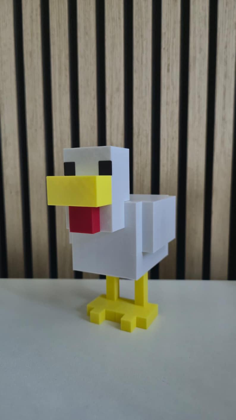 May include: A blocky, pixelated chicken figurine constructed from white, yellow, and red plastic components. The figure features a white body and head, a prominent yellow beak, a red wattle, black square eyes, and yellow feet with three toes.