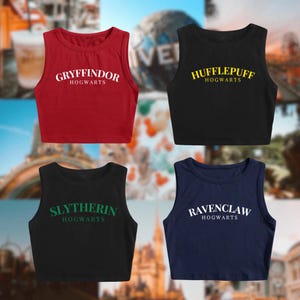 May include: Four sleeveless crop tops in red, black, and navy blue. Each top features a different Hogwarts house name in white or yellow lettering: Gryffindor, Hufflepuff, Slytherin, and Ravenclaw. The tops are displayed against a blurred background.