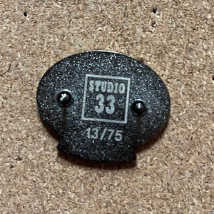 May include: Black and white pin with the text "Studio 33" and the number "13/75" printed on it.