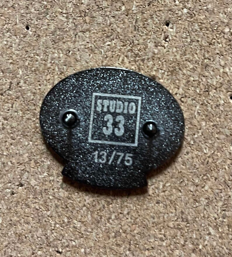 May include: Black and white pin with the text "Studio 33" and the number "13/75" printed on it.