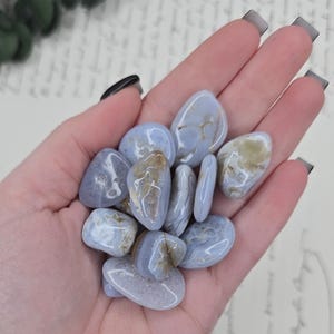 Puede incluir: Un pu&ntilde;ado de piedras pulidas de &aacute;gata de encaje azul. Las piedras son de color azul p&aacute;lido con inclusiones blancas y beige. Las piedras son lisas y redondeadas, y parecen haber sido pulidas. El fondo es un papel vintage.