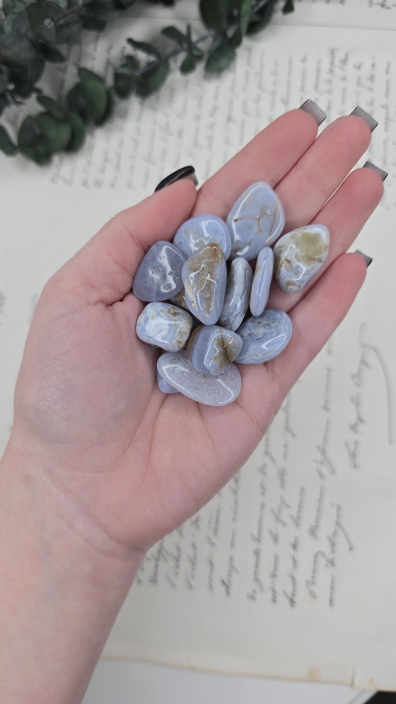 Puede incluir: Un pu&ntilde;ado de piedras pulidas de &aacute;gata de encaje azul. Las piedras son de color azul p&aacute;lido con inclusiones blancas y beige. Las piedras son lisas y redondeadas, y parecen haber sido pulidas. El fondo es un papel vintage.