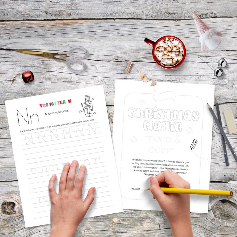 May include: A festive scene with two activity sheets featuring the text "The Letter N" and "Christmas Magic". A hand holds a yellow pencil, coloring the "Christmas Magic" sheet. Other items include scissors, a mug of cocoa, and holiday decorations.