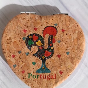 Op de afbeelding: Een hartvormige kurken sieradendoos met een kleurrijk haanontwerp en het woord "Portugal" gedrukt op de voorkant.