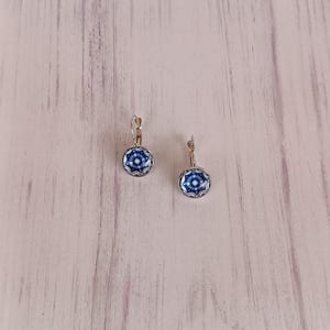Pode incluir: Um par de brincos de pressão prateados com cabochões de vidro com padrões azuis e brancos.