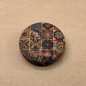 Könnte beinhalten: Ein runder, korkbeschichteter Anhänger mit einem bunten, gemusterten Design aus geometrischen Formen und floralen Motiven. Der Anhänger trägt die Aufschrift "Portugal" in roten Buchstaben.