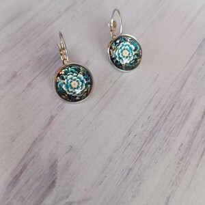 Op de afbeelding: Een paar zilveren oorbellen met een blauw en wit bloemenmotief. De oorbellen zijn rond en hebben een zilveren haak.