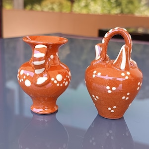 Pode incluir: Dois jarros pequenos de cerâmica marrom com bolinhas brancas. Os jarros têm um design tradicional e são perfeitos para fins decorativos.