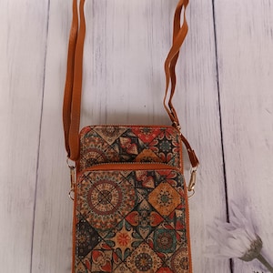 May include: A rectangular crossbody bag with a brown leather strap and a patterned front. The pattern features a mix of red, orange, green, and blue geometric shapes. The bag has a gold zip and a brown leather trim.