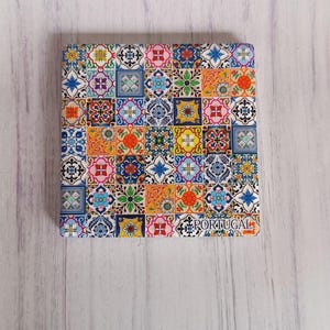 Könnte beinhalten: Ein bunter Untersetzer mit einem geometrischen Muster aus blauen, grünen, gelben, orangen, roten und weißen Fliesen. Der Untersetzer hat den Schriftzug "PORTUGAL" auf der Unterseite.