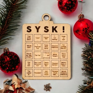 May include: A wooden Christmas ornament with the text "SYSK!" and a grid of squares containing phrases related to the podcast "Stuff You Should Know".