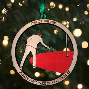 May include: Wooden Christmas ornament with a circular design. The ornament features a figure reaching towards a red object, with the text "JUSTICE FOR JOE" and "PLEASE DON'T TAKE IT AWAY FROM ME" in a circular pattern. A green ribbon is attached for hanging.